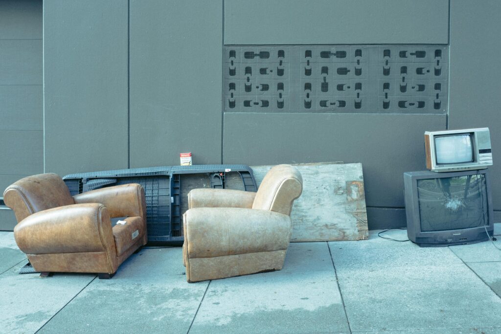 Sidewalk scene with vintage chairs and old televisions against a wall.